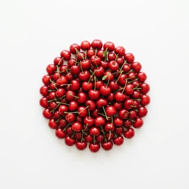 A round pile of fresh red cherries with their stalks on a plain white background