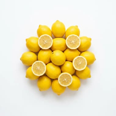 A round pile of yellow lemons with several cut halves, on a plain white background