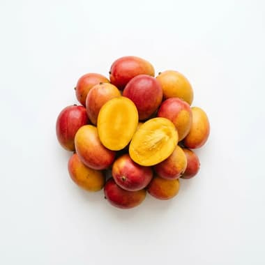 A round pile of ripe red and yellow mangoes with one sliced open, on a plain white background