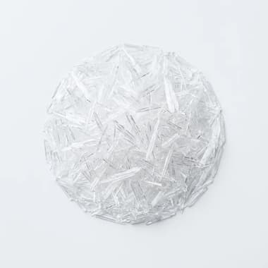 A round pile of clear, needle-shaped menthol crystals on a plain white background