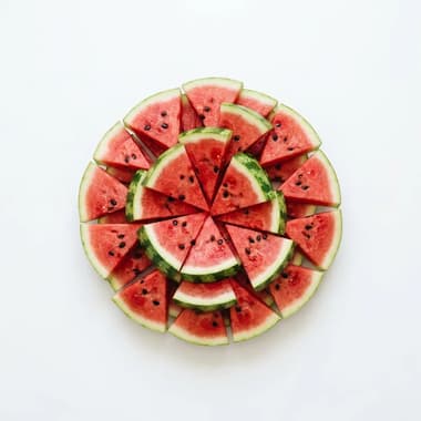 A round arrangement of fresh watermelon wedges on a plain white background